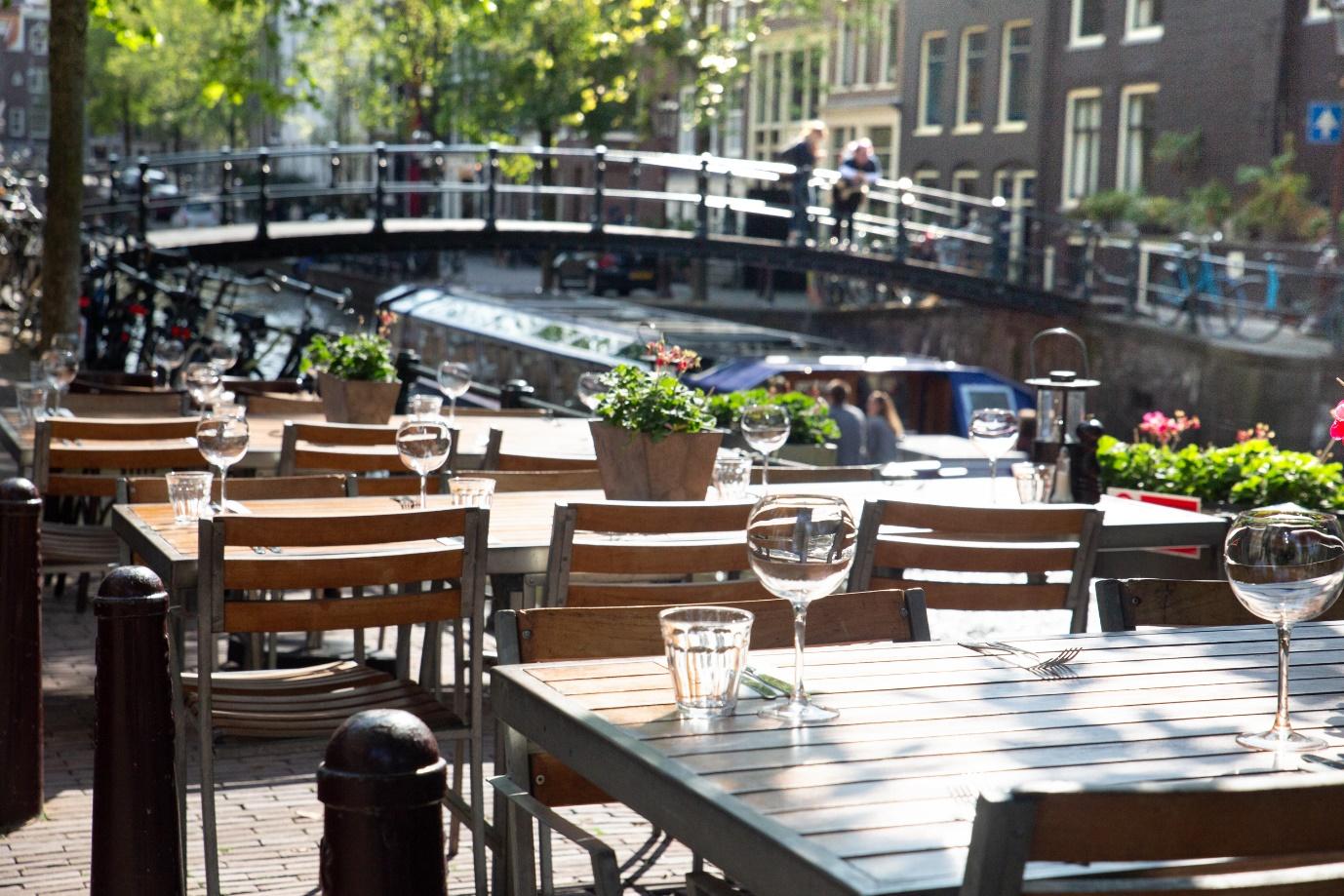Amsterdam restaurant cafe tables set for outdoor dining with glassware and view of canal bridge in the background